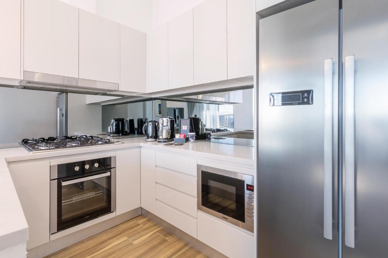Meriton Suites Bondi Junction Sydney Kültér fotó The photo shows a modern kitchen with a clean and minimalist design. It features white cabinetry and a stainless steel refrigerator. The kitchen includes a gas stove with an oven below it, as well as a microwave. There are several kitchen appliances,
