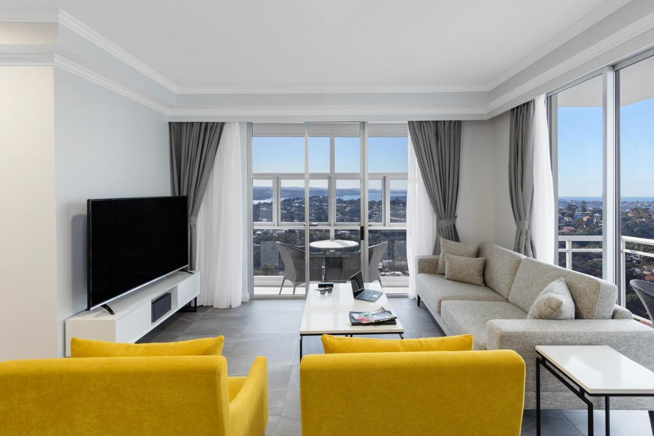 Meriton Suites Bondi Junction Sydney Kültér fotó The photo depicts a modern living room space with large windows that offer a view of the outside. The decor is minimalist and stylish, featuring a light color palette. 

In the center, there are two bright yellow chairs facing each other. A sleek, re