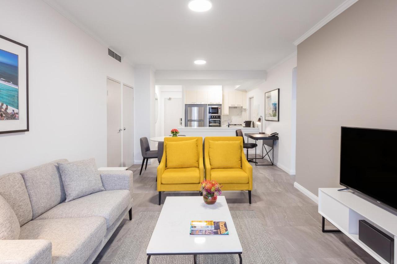 Meriton Suites Bondi Junction Sydney Kültér fotó The photo shows a modern living space with a light and airy design. In the foreground, there are two bright yellow armchairs flanking a white coffee table, which has a small vase of flowers and a magazine on it. To the left, there is a light gray sof