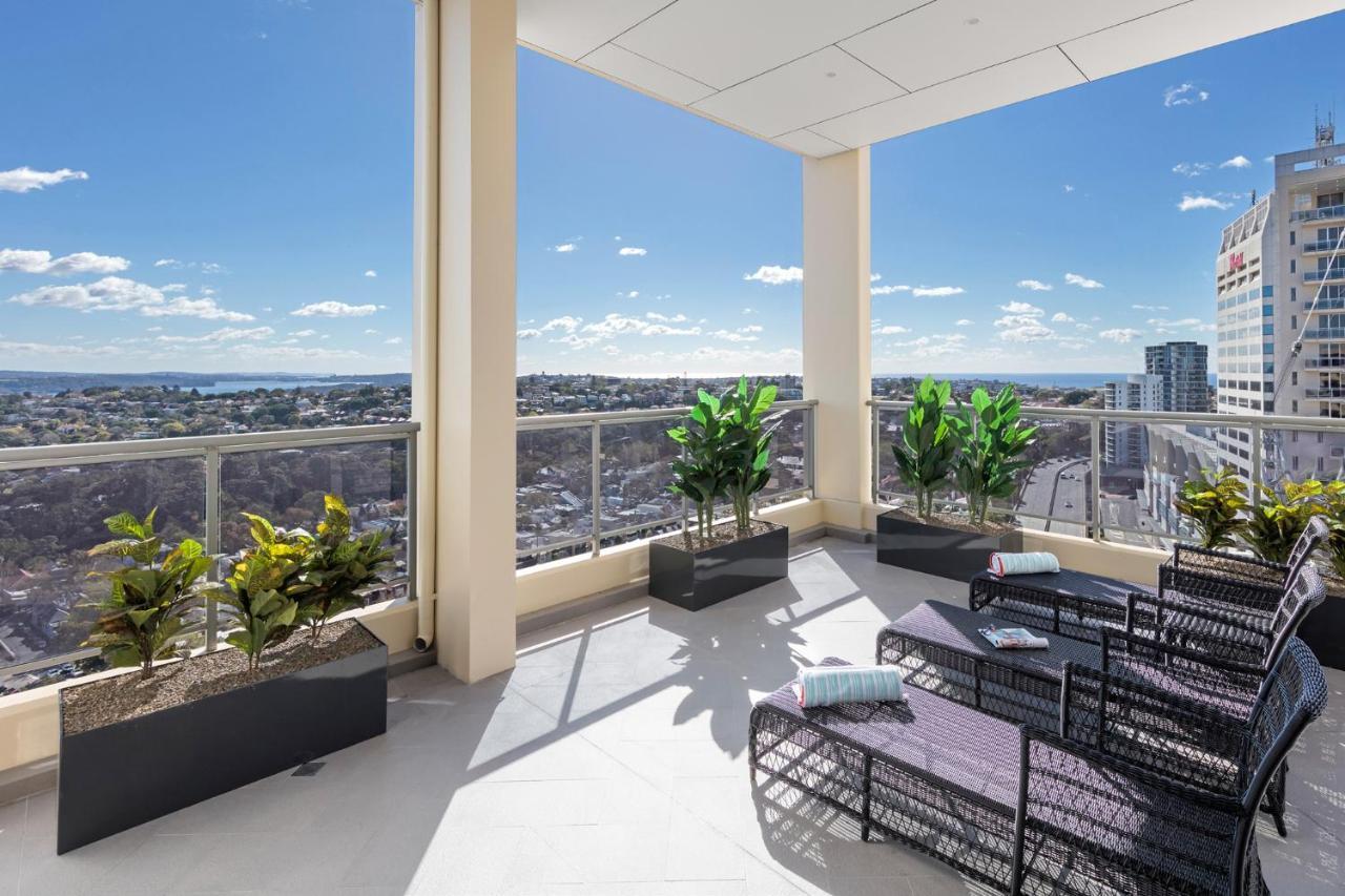 Meriton Suites Bondi Junction Sydney Kültér fotó The photo shows a modern balcony or terrace area with a stunning view. There are several planters with green plants placed along the edge. The seating area features lounge chairs in a contemporary design, likely made of woven materials. The space app