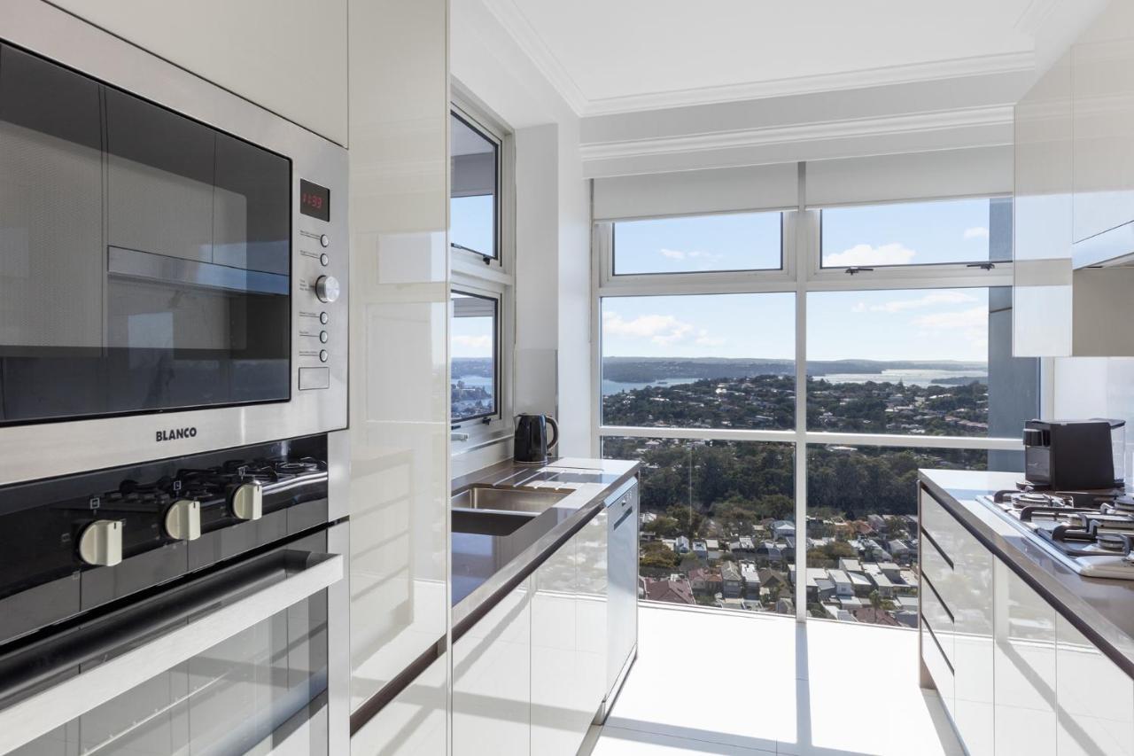 Meriton Suites Bondi Junction Sydney Kültér fotó The photo shows a modern kitchen with sleek, shiny white cabinets and a large window that offers a panoramic view of the outside landscape. The kitchen features built-in appliances, including an oven and a stove, with a stylish countertop. The spacio