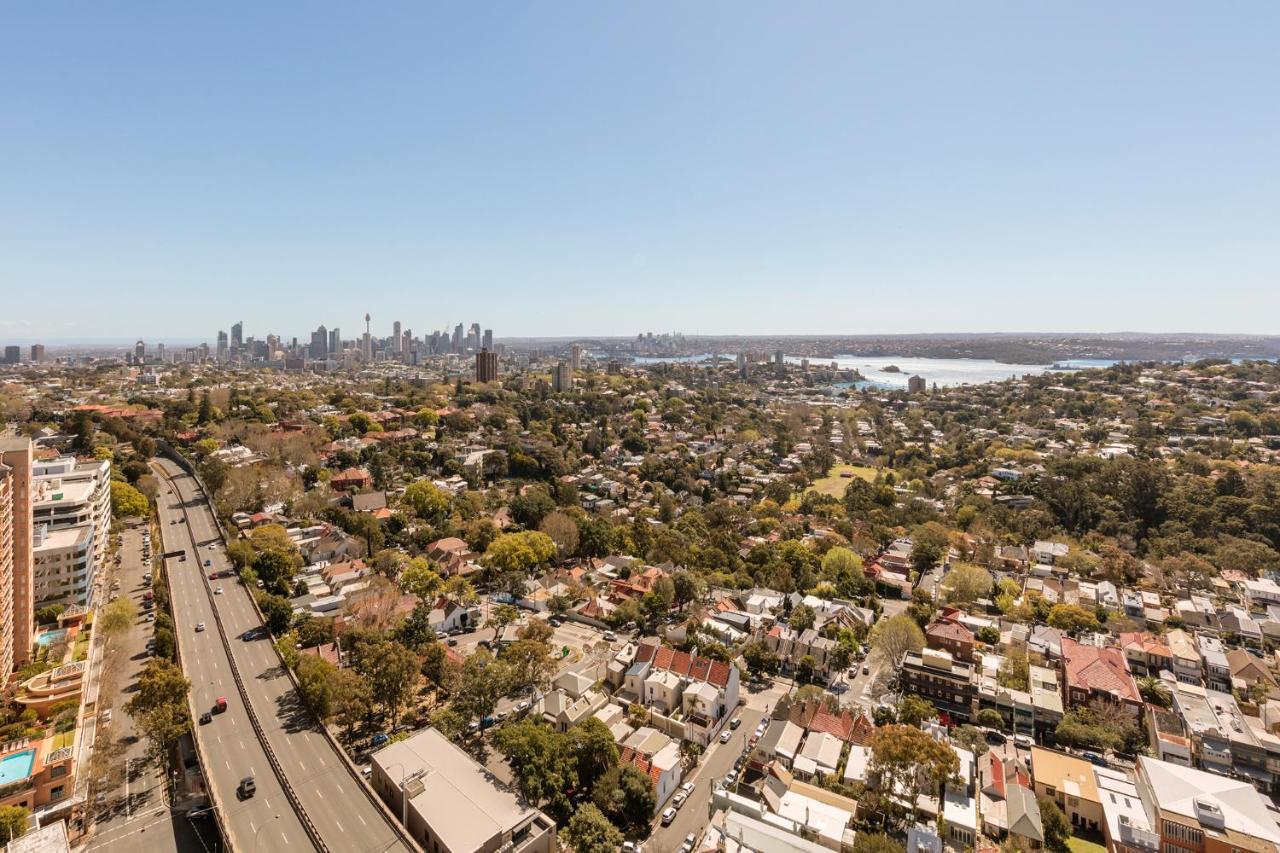 Meriton Suites Bondi Junction Sydney Kültér fotó The photo captures a panoramic view of a vibrant urban landscape. In the foreground, there are residential areas with various houses and greenery, showcasing a suburban environment. In the background, the skyline of a city can be seen, featuring tall