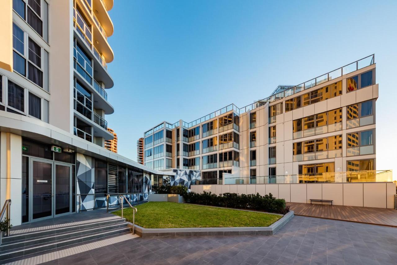 Meriton Suites Bondi Junction Sydney Kültér fotó The photo showcases a modern residential area featuring contemporary buildings. In the foreground, there is a landscaped green space surrounded by well-designed architecture. The buildings have large glass windows, reflecting the light, and feature a