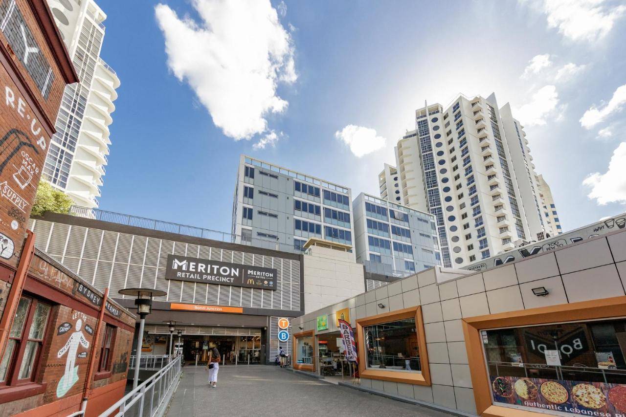 Meriton Suites Bondi Junction Sydney Kültér fotó The photo depicts a modern urban environment featuring a building labeled "Meriton Retail Precinct." In the foreground, there are shops with colorful signage, while in the background, tall residential buildings tower over the area. The sky above is b