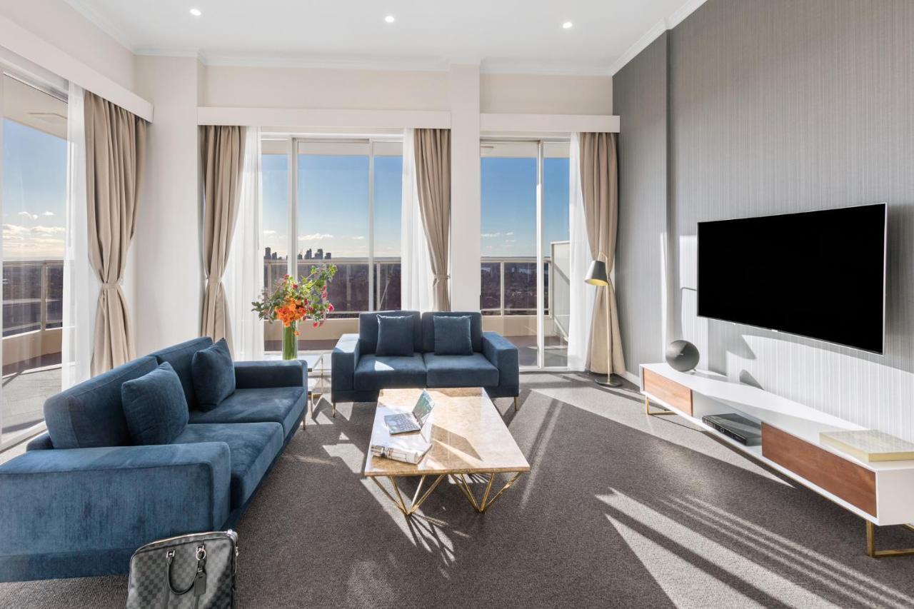 Meriton Suites Bondi Junction Sydney Kültér fotó The photo depicts a modern living room with a stylish and contemporary design. It features a cozy seating arrangement with a blue sofa and two matching armchairs. In front of the seating area is a coffee table with a geometric design. The room has la