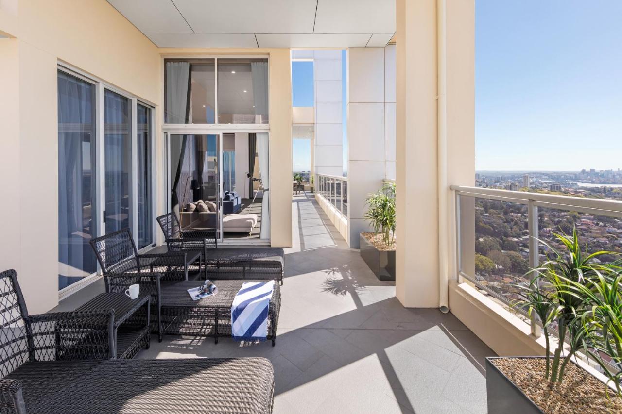 Meriton Suites Bondi Junction Sydney Kültér fotó The photo shows a spacious balcony or terrace area of a high-rise building. It features modern outdoor furniture, including a seating arrangement with dark wicker chairs and a table. There are cushions, and a blue and white striped blanket is draped 